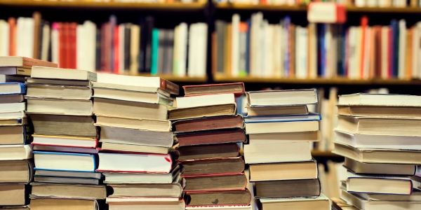 stacks of used books piled on a table with more loaded on shelves behind