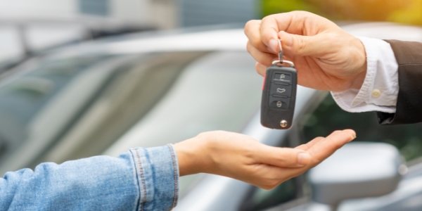 one hand giving car keys to another hand with a car in the background