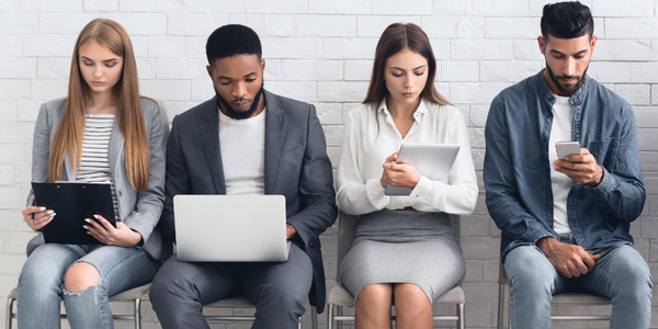 four people seated in chairs looking at laptops and devices