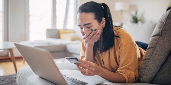 adult looking dismayed at a laptop and holding a credit card