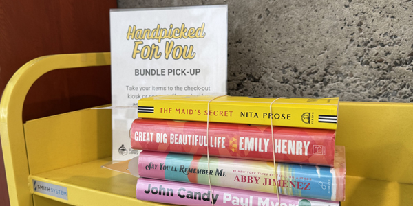 stack of books on a book truck beside a Handpicked For You sign