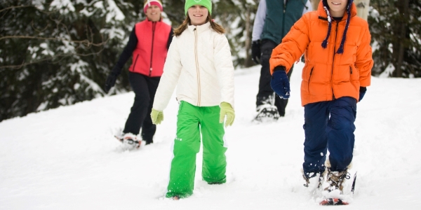 four people walking in snow using snowshoes