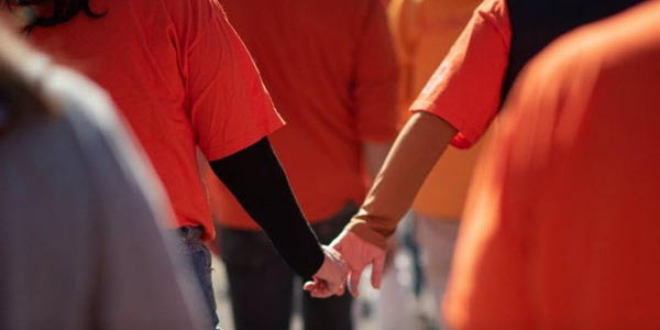 two people wearing ornange shirts and holding hands