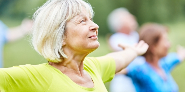 older adult with outstretched arms in a yoga pose with other adults in background