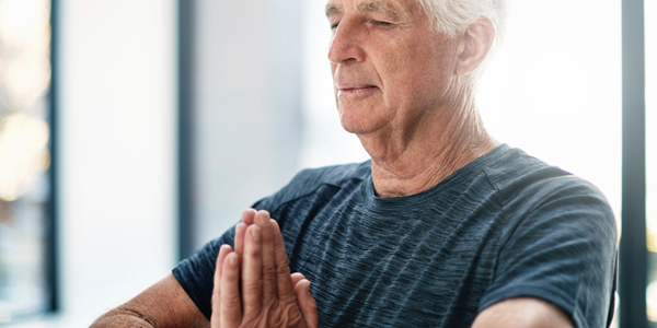 older man with closed eyes holding hands in yoga prayer position