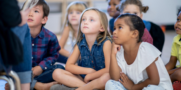 group of children seated on the floor looking up at an adult 