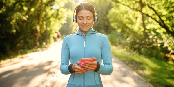 adult standing outside looking at a mobile phone and wearing headphones