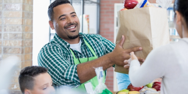 man handing over a full grocery bag to a woman