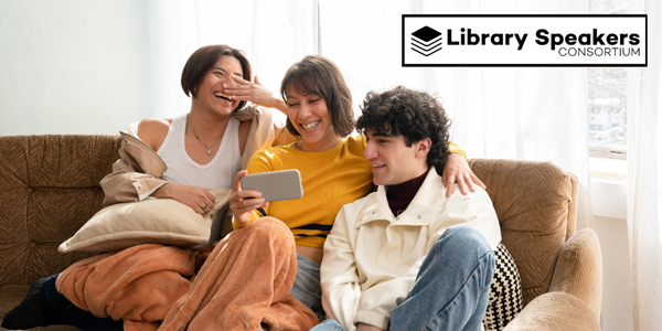 three smiling adults sitting on a couch looking at a mobile phone