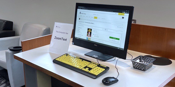 computer monitor, mouse, and large print keyboard, with Zoom Text sign in background