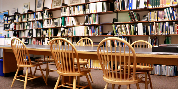 large wood table with five chairs in front of a wall of book shelves inside the local history room