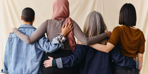 four people of various cultures and communities facing away with their arms around eachother's shoulders