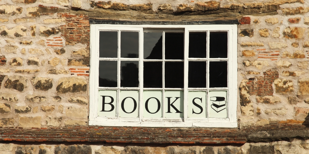 exterior of an old stone building with a window with a sign saying Books below it