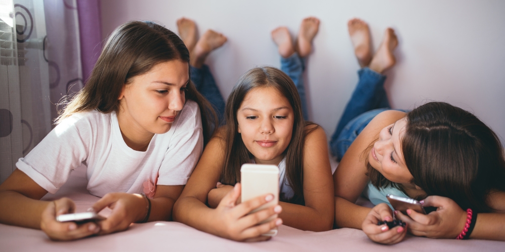 three youth laying on a bed holding mobile phones