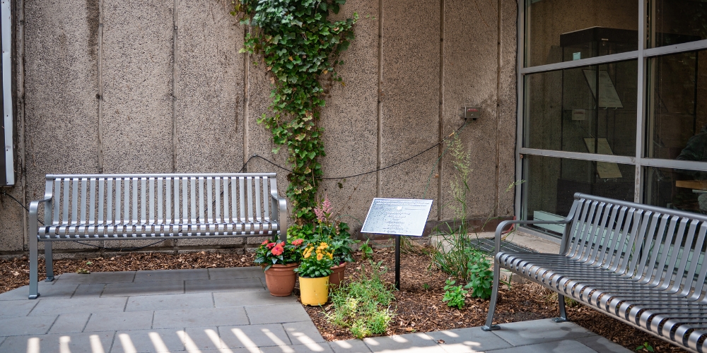A plaque listing garden donors is flanked by two benches in a corner of the garden