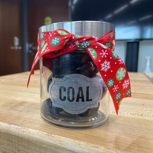 A glass jar with coal inside with the word "Coal" engraved on the front