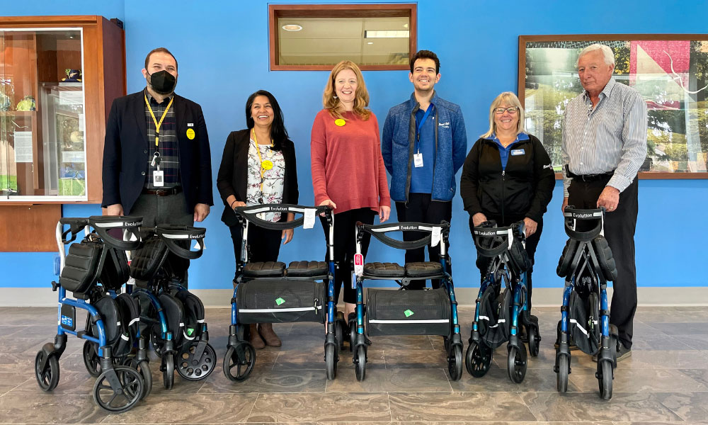 A group stands in front of a blue wall displaying the rollators