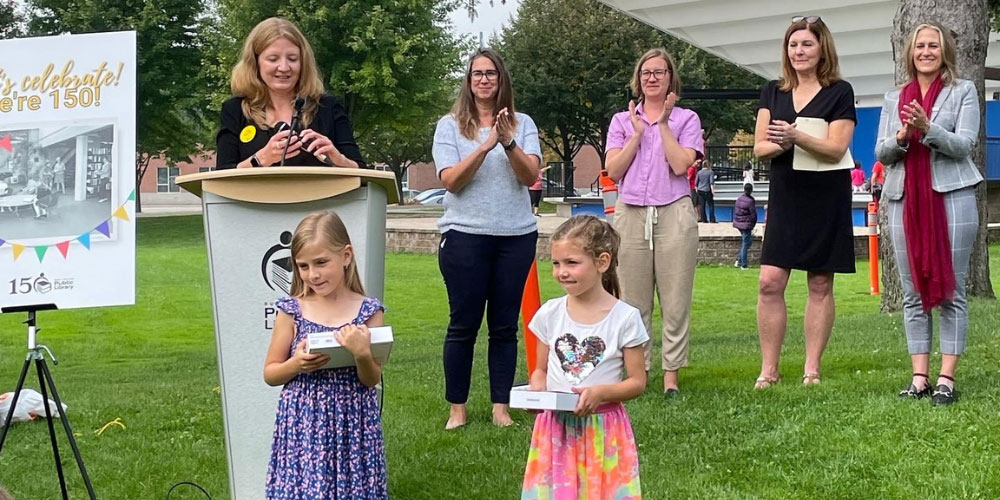 Two young girls stand in front of a podium with a lineup of women behind them