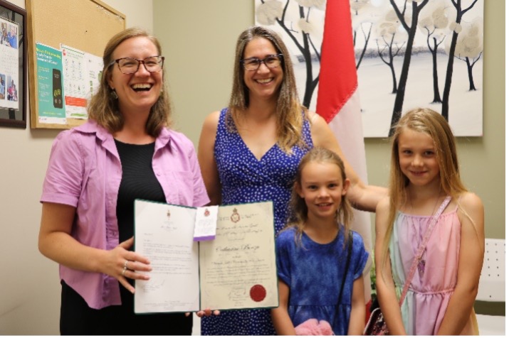 MP Karina Gould presents a folder to Catharine Benzie with her two daughters in front