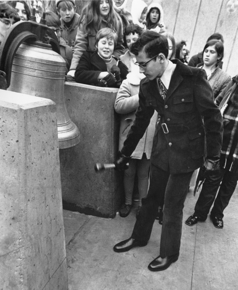 Michael Rose striking the bell in 1970 surrounded by a crowd of people