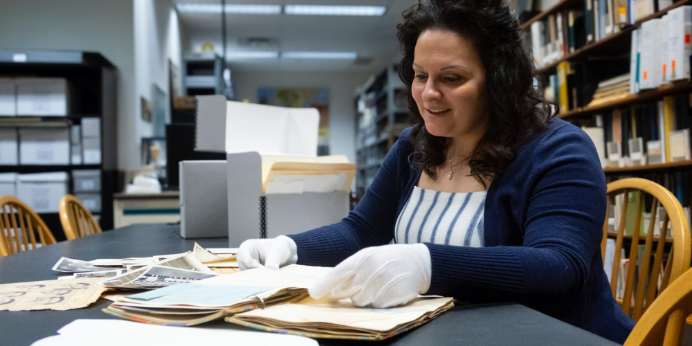 Marisa Purdy seated at a table looking at various archival items in BPL's Burlington History Room