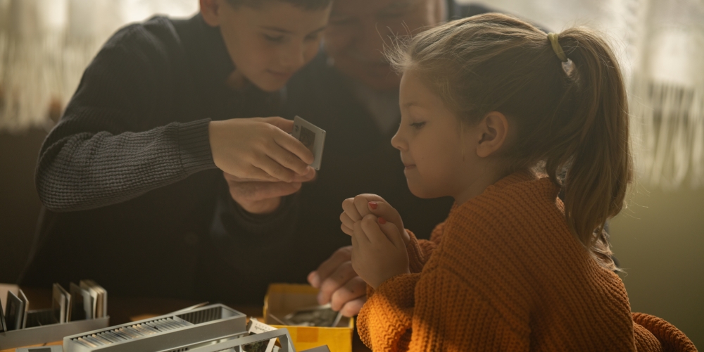 two young children looking at old photo slides with an elderly person