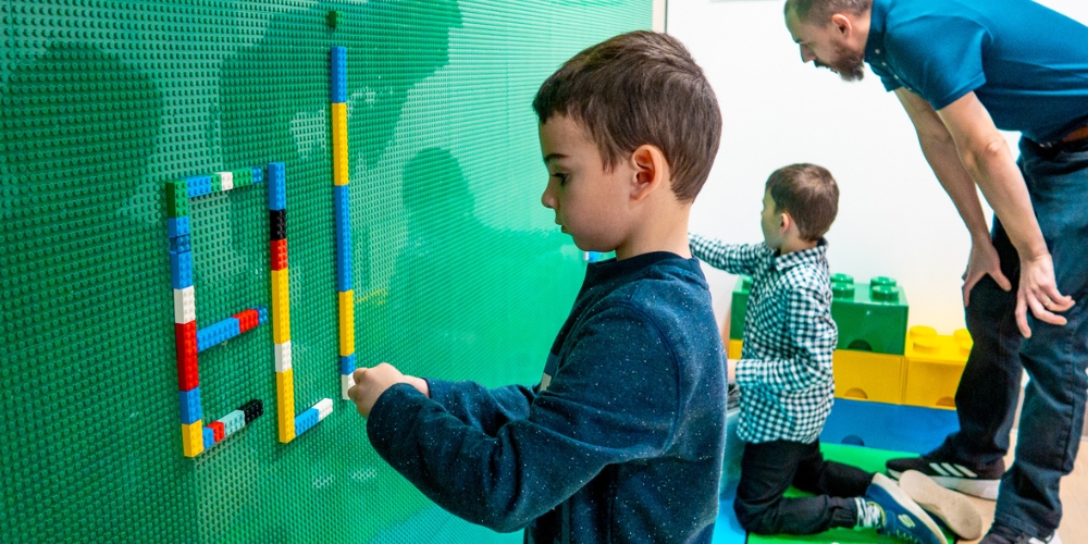 adult with two children playing at the LEGO wall in the DiscoverySpace at Central