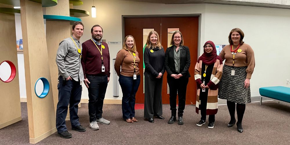 A group photo of Minister Karina Gould and library staff outside one of the program room door openers