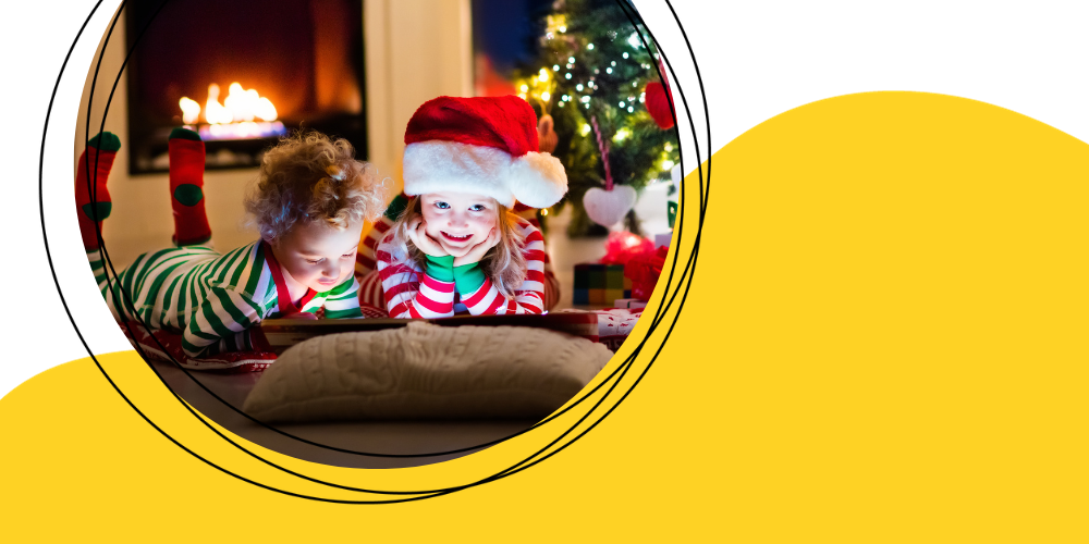  Two young kids in pajamas reading a book. One child is wearing a santa hat.