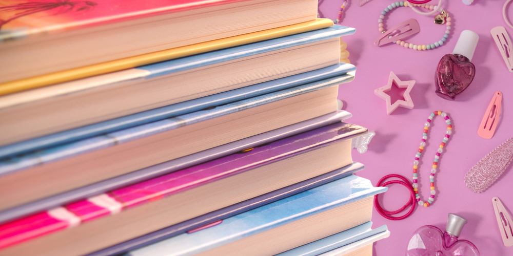 Pink background with hair clips and nail polish. Stack of books in the foreground.