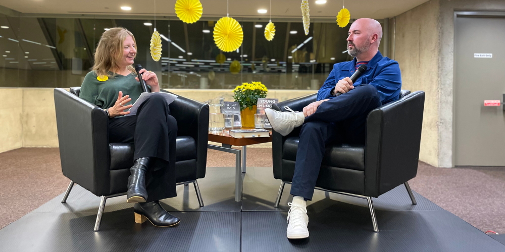 CEO Lita Barrie and Douglas Stuart sit in arm chairs on a stage, facing each other