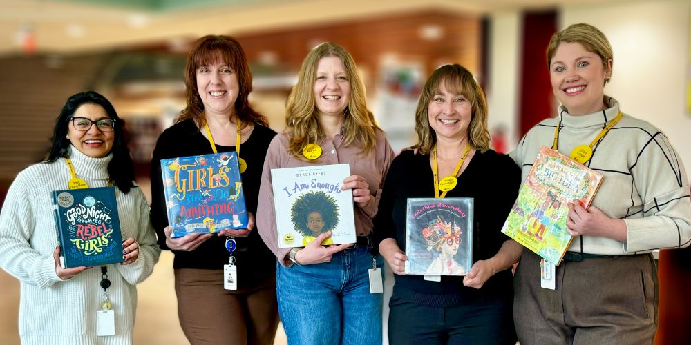 Five women standing in a row holding books: Meg Uttangi Matsos with Good Night Stories for Rebel Girls, Cindy Tchorz with Girls Can Do Anything, Lita Barrie with I Am Enough, Nicole Tewkesbury with Girls Think of Everything, and Elise Copps with Kamala and Maya’s Big Idea 