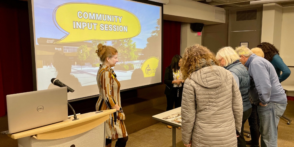 Several people gather around a table looking at mockup designs of the library branch.