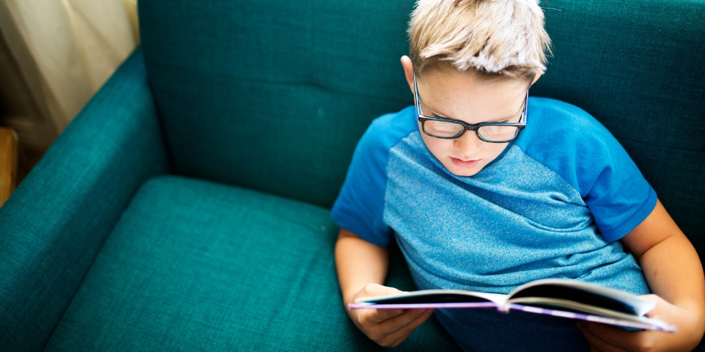 school-age child sitting on a couch reading a book