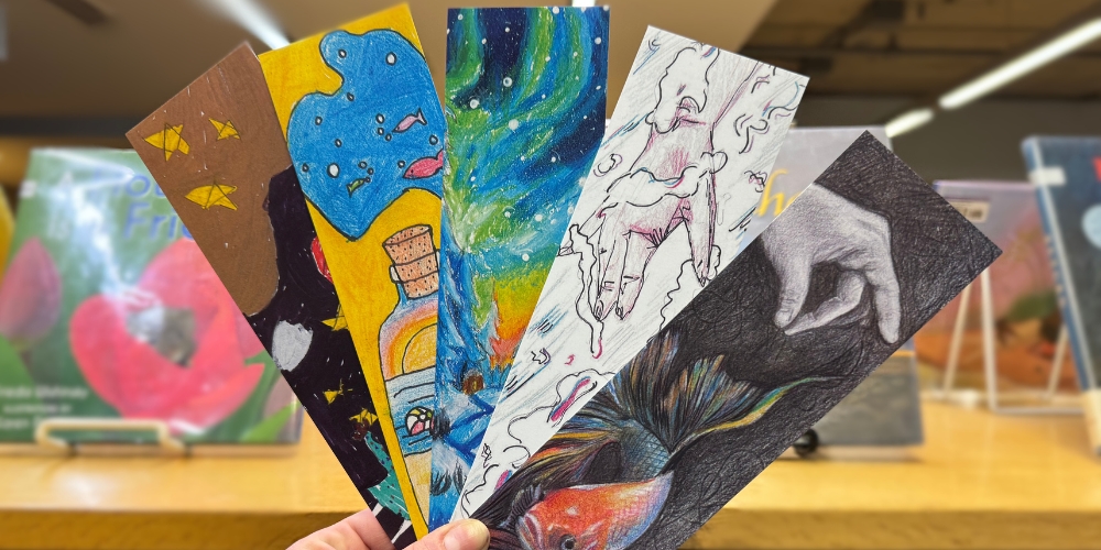 A hand holding up five colourful, hand drawn bookmarks