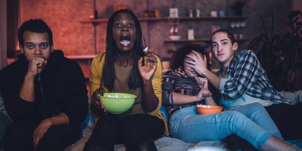 four adults seated on a couch facing the viewer with looks of horror on their faces