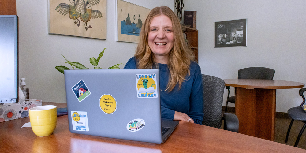 BPL CEO, Lita Barrie, smiles at the camera from behind a laptop.