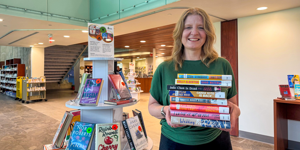 BPL CEO Lita Barrie standing in Central Branch lobby and holding up a stack of books