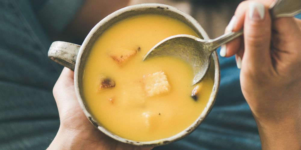 hands holding bowl of squash soup with croutons and spoon