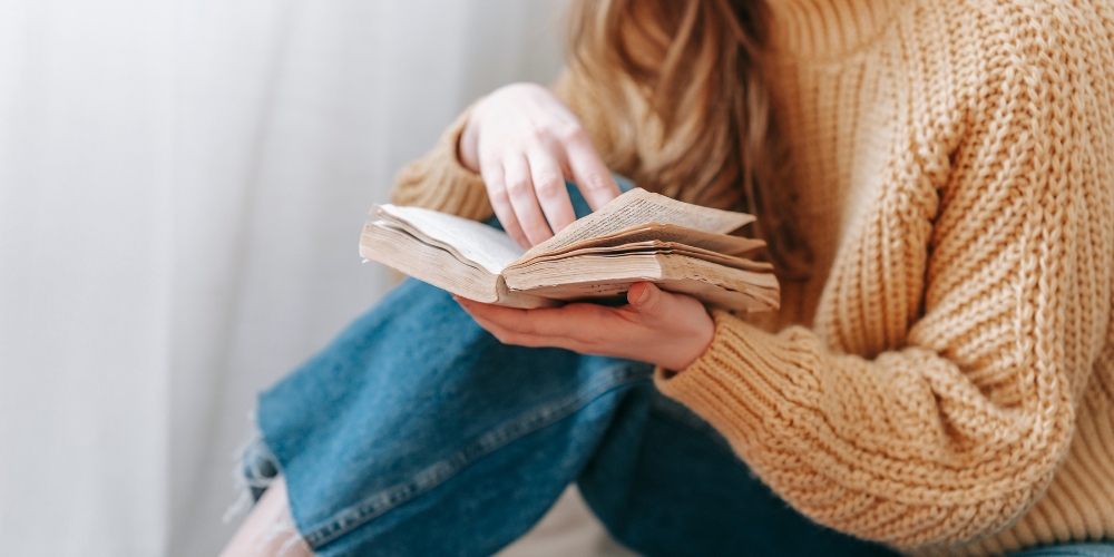 seated woman holding an open paperback book in her hand