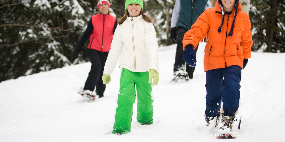 four people walking in snow using snowshoes