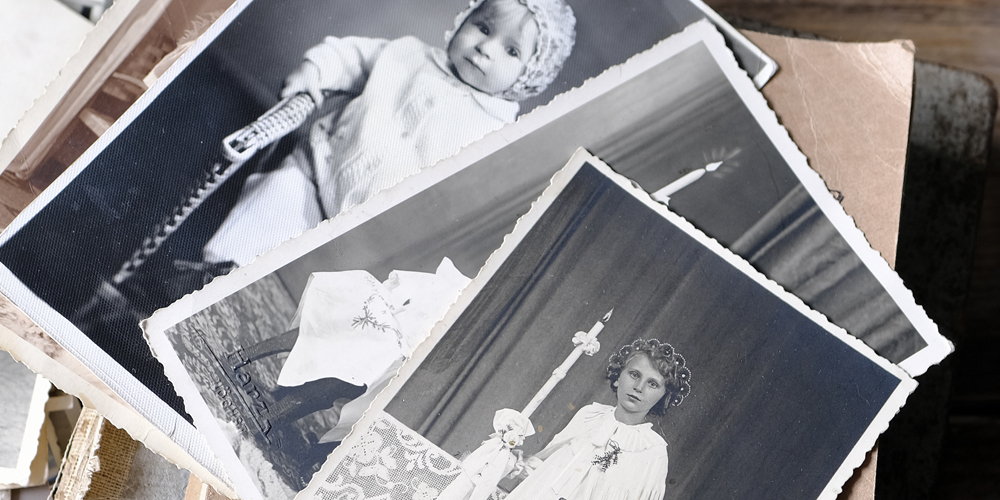 stack of many old photos spread on a table with two black and white photos of children taken about a century ago