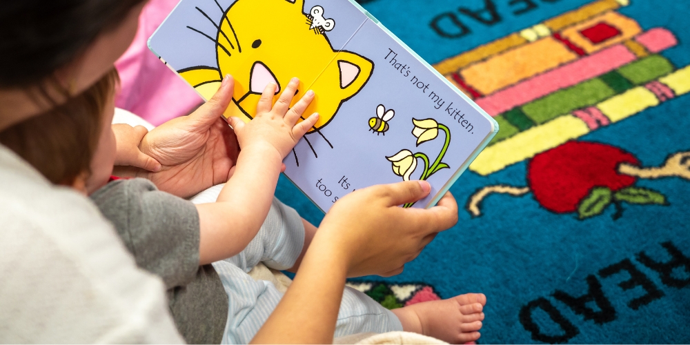 adult with child in their lap reading a board book together at the library