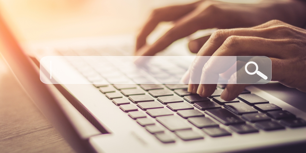 hands typing on a computer keyboard with a search field and icon superimposed on top