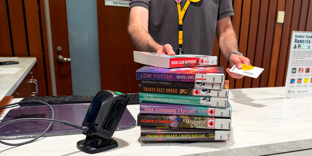 staff holding library card near a stack of books at the checkout desk