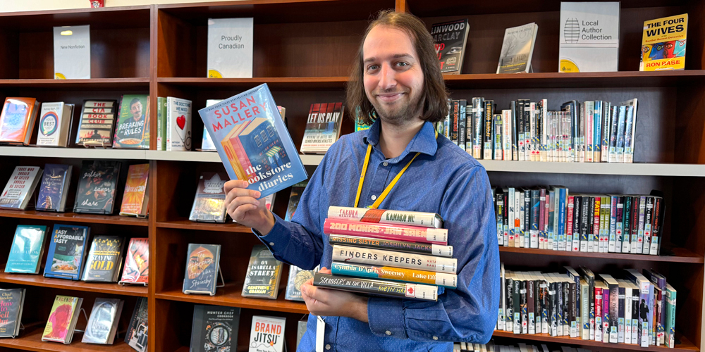 BPL staff member holding up a book in their right hand and a stack of books in their left