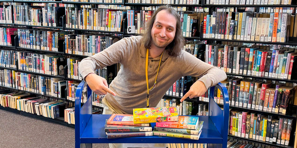 staff leaning against a book truck with stack of new books