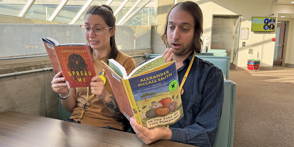 two adults sitting at a table, each holding a book