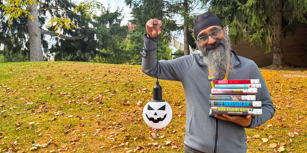 staff member standing outside holding a stack of books and a Halloween decoration