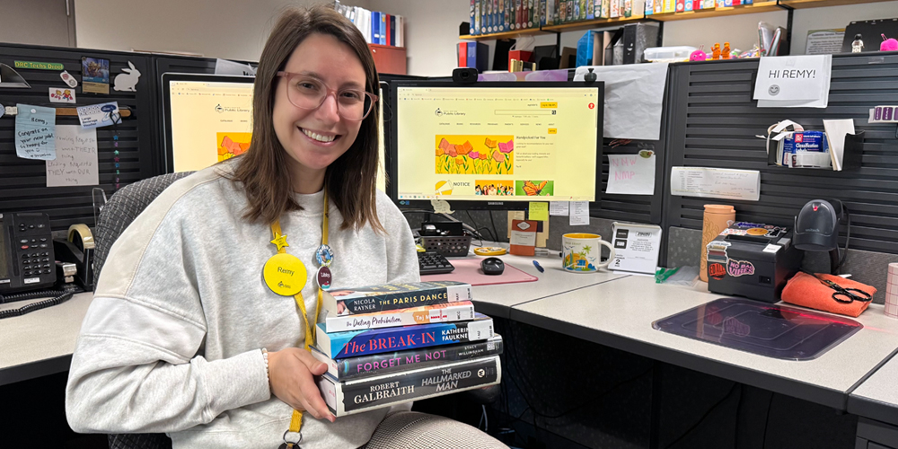 smiling staff member holds a stack of five books